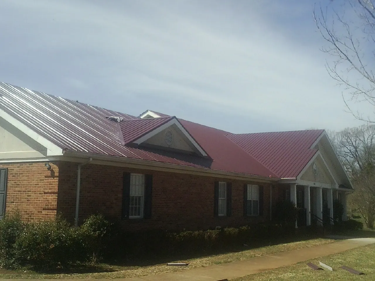 Red metal roof with gabled entries on a long brick building, from a Hail Damage Roof Repair job in Caledonia