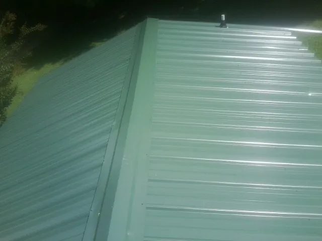 New green metal panels meeting at the ridge of a roof — Flat Roof Repair work by our crew in Caledonia